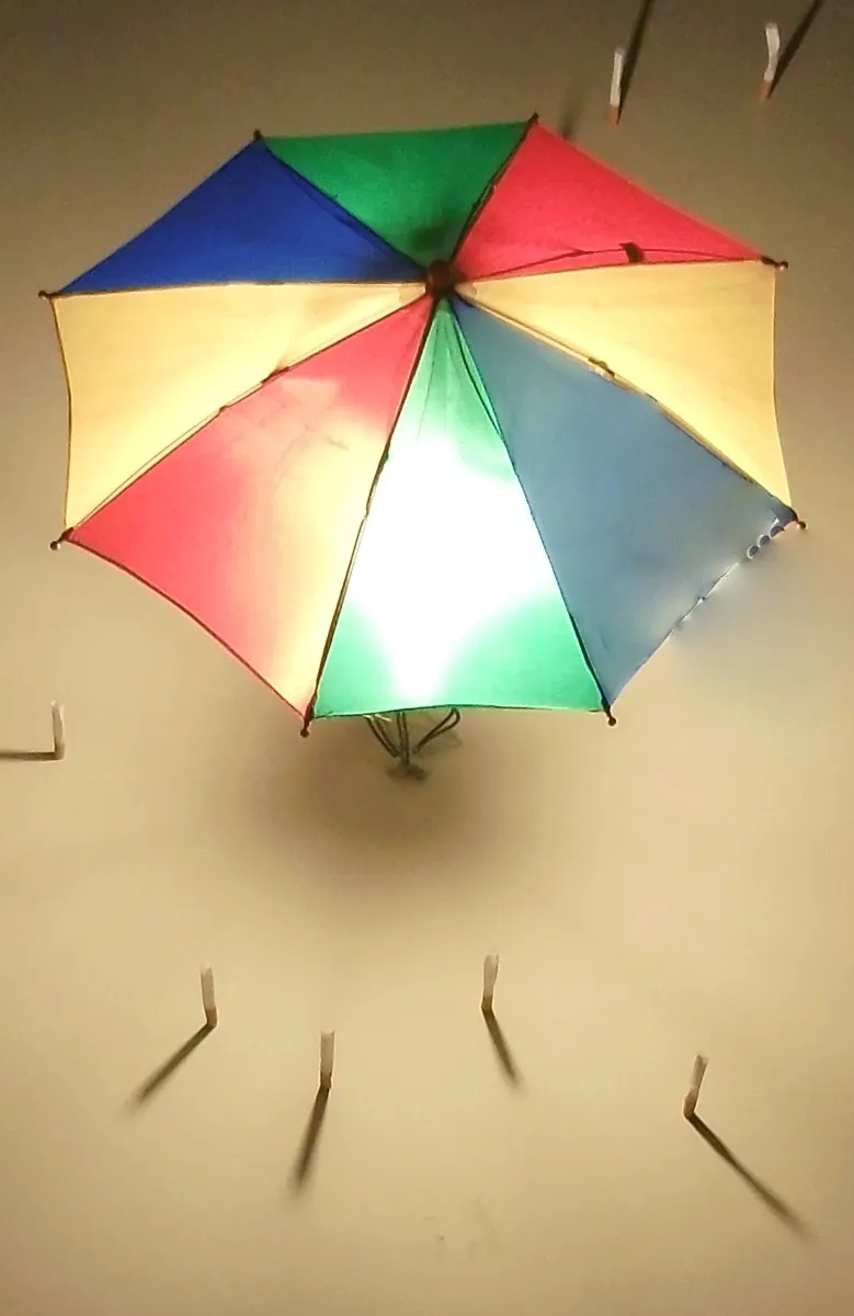 Lit rainbow umbrella mounted on a wall with nails radiating around it
